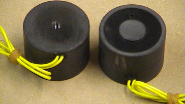 To sorte elektriske komponenter med gule ledninger, der står på en beige overflade.