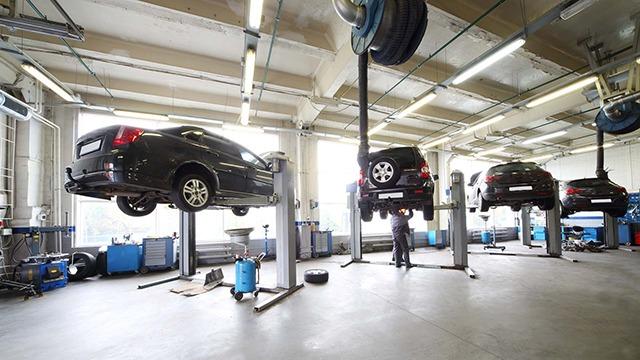 Et moderne autoværksted med flere biler hævet på lift, mekanikere arbejder på reparationer.