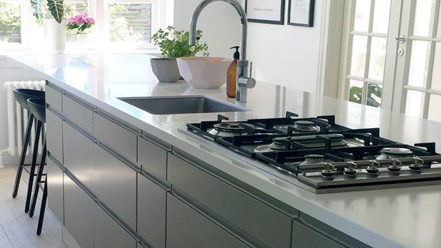 Moderne køkken med en grå køkkenø, gaskogeplade og planter i potter på bordet.