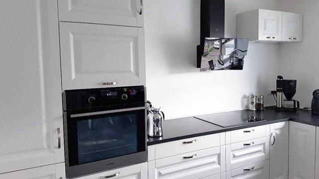 Moderne køkken med hvide skabe, indbygget ovn og sort bordplade, samt en væghængt emhætte.
