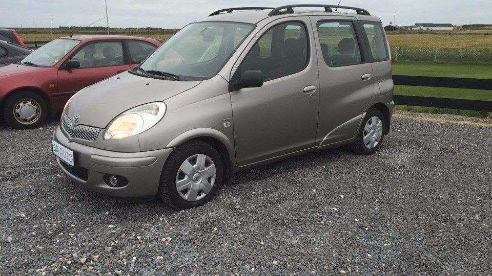 En sølvgrå minivan parkeret på en grusvej med grønne marker i baggrunden.