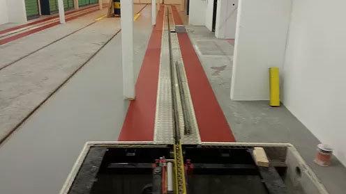 Billede af en tom garage med røde og grå gulve, hvor der er spor til køretøjer.