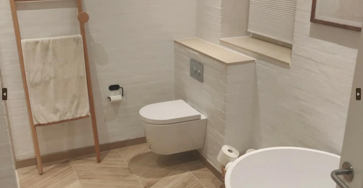 Moderne badeværelse med toilet, håndklædestativ og badekar i lyse farver og trædetaljer.