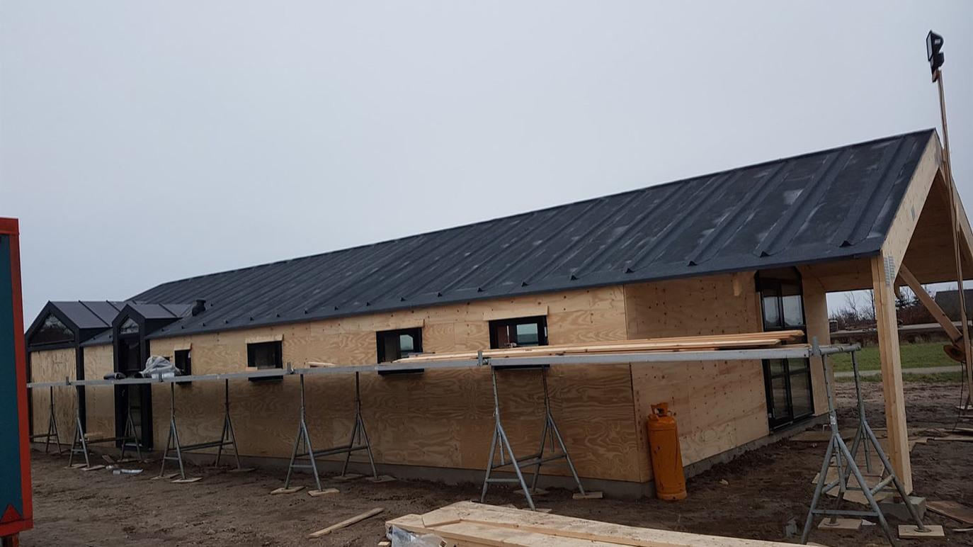 Nybygget hus med sort tag og træfacade, omgivet af stilladser på en byggeplads.