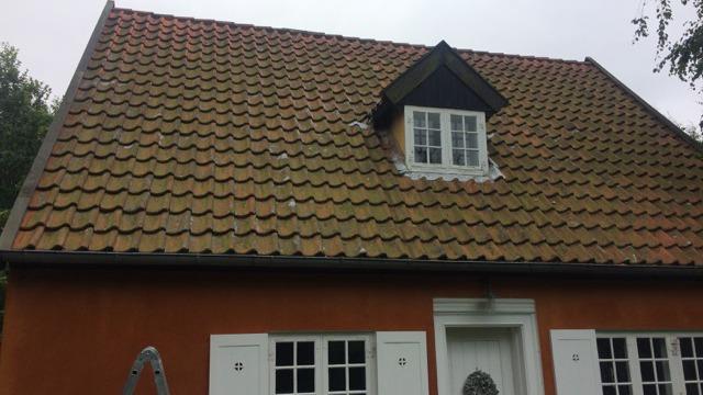Taget på et hus med teglsten og en kvistvindue, malet i orange med hvide døre.