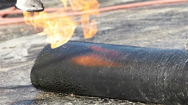 Flamme, der brænder på en sort rulle, med røg og glødende overflade i baggrunden.
