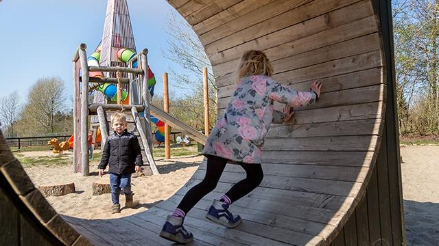 Børn leger på legepladsen; en pige klatrer på en træstruktur, mens en dreng ser på.