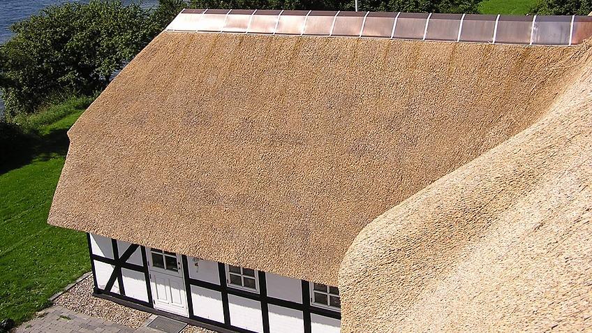 Et stråtækt hus med hvid facade og sort bindingsværk, set fra oven. Græsplæne i baggrunden.