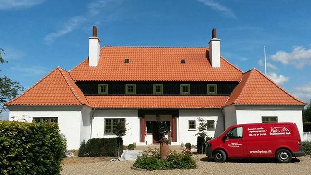 Et stort, hvidt hus med rød teglstenstag og en rød varevogn parkeret foran.