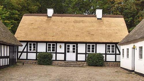 Et charmerende stråtækt hus med hvidkalkede vægge og sorte bindingsværk i en naturskøn indstilling.