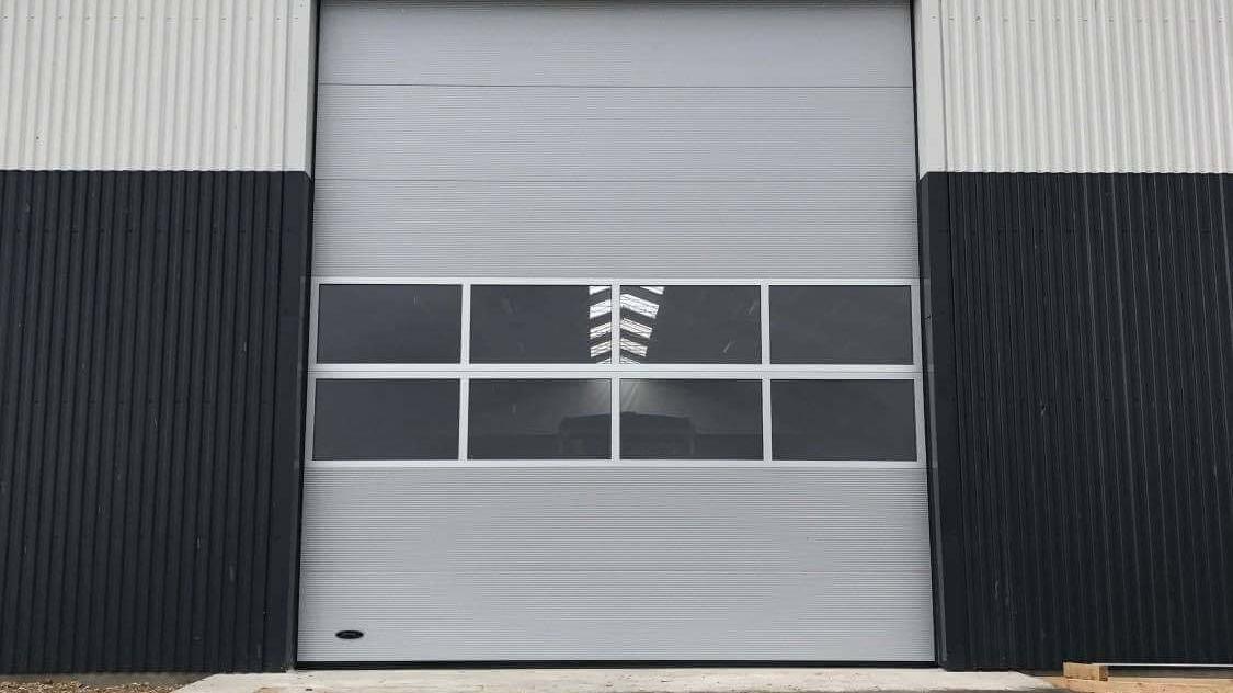 En stor grå garageport med vinduer, placeret på en bygning med sort og grå facade.