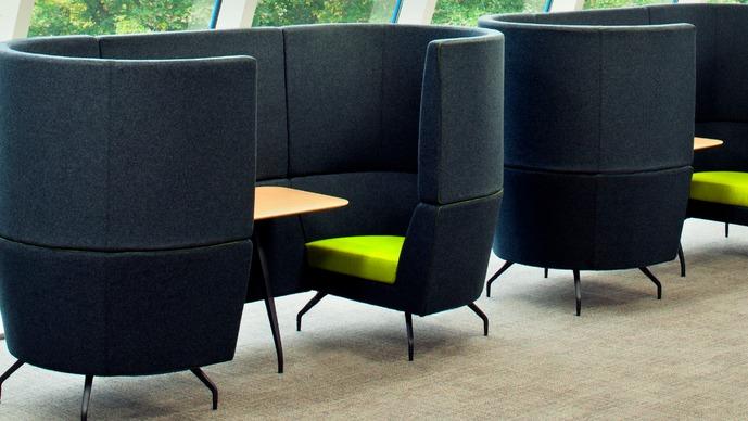Moderne, høje sofaer med grønne sæder og borde i et lyst kontormiljø.