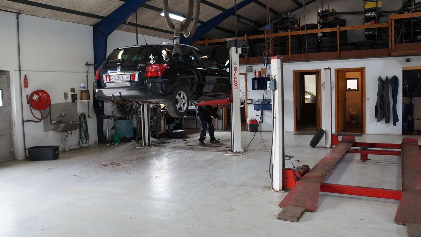 Bileftermarked værksted med en hævet bil og mekaniker, der arbejder på bilen i en rummelig garage.