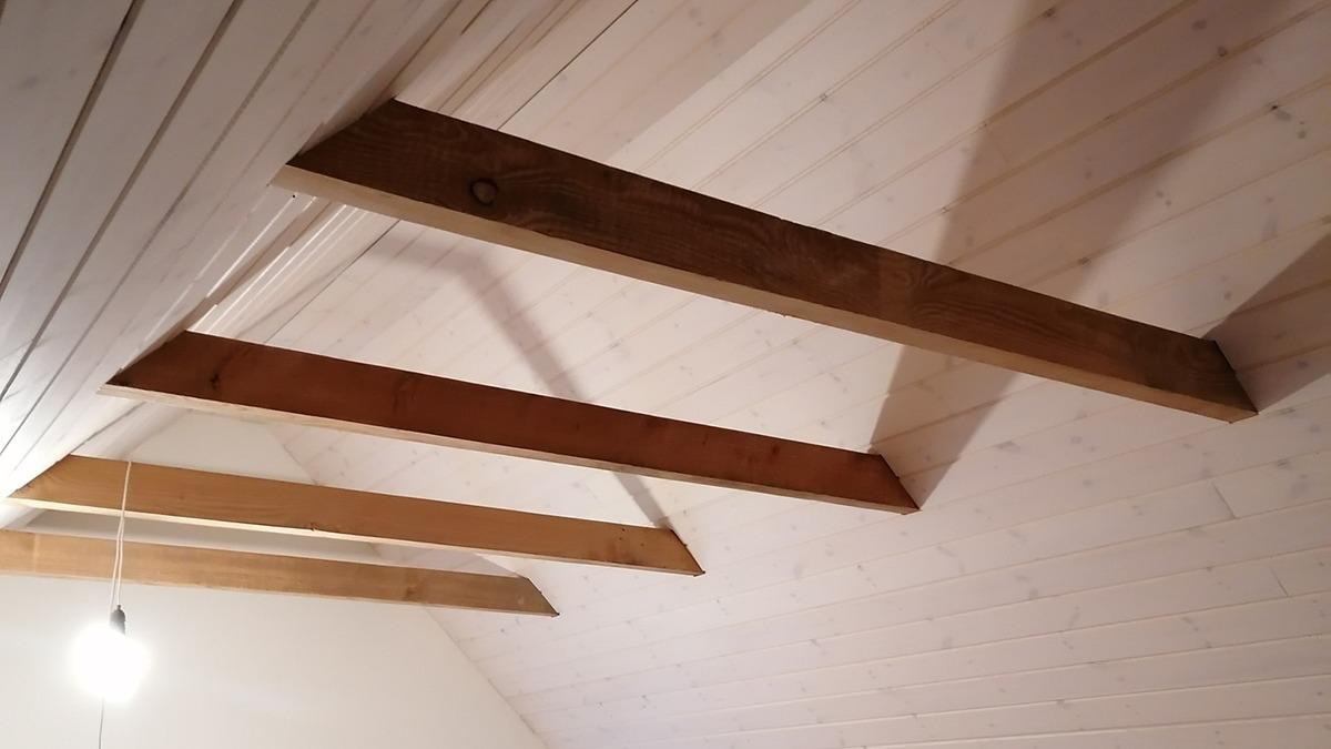 Loft med synlige træbjælker og en lampe hængende i rummet.