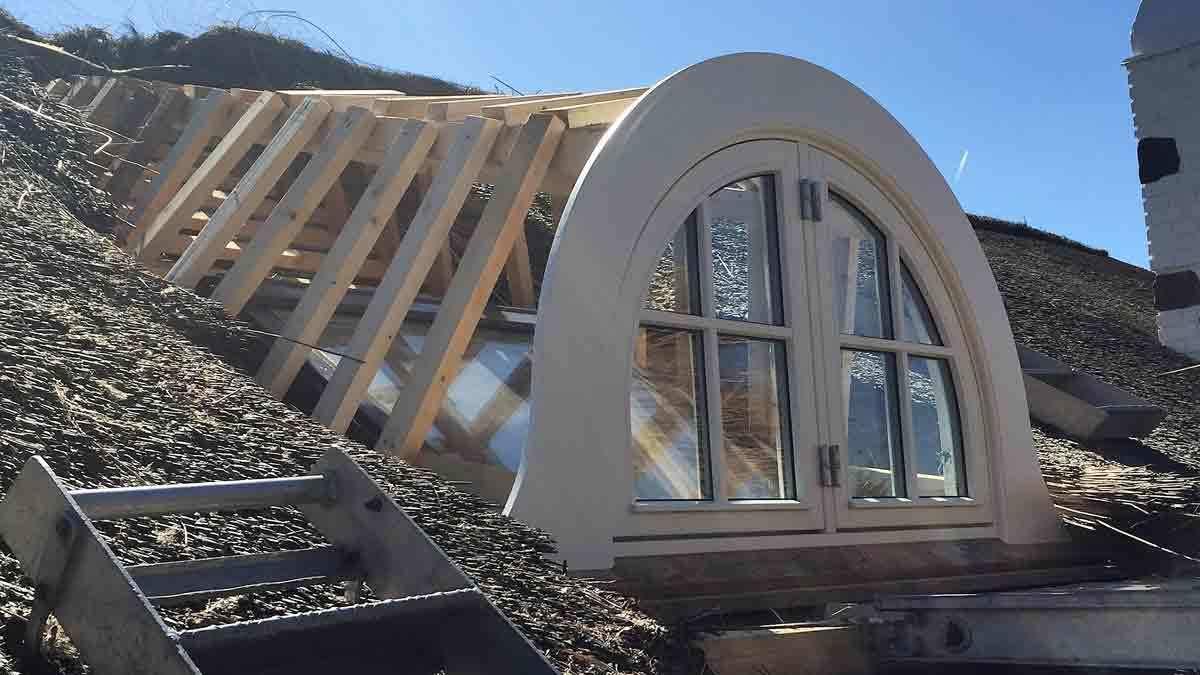 Et vindue i en skråtag med træramme og grusbelægning under en klar blå himmel.