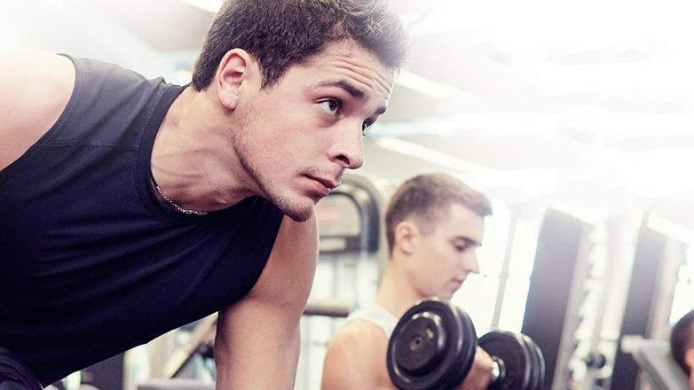 To mænd træner i et fitnesscenter, den ene løfter håndvægte og fokuserer intenst på sin træning.