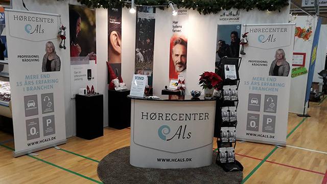 Hørecenter A/S messestand med bannere, informationsmateriale og dekorationer i en sportshal.