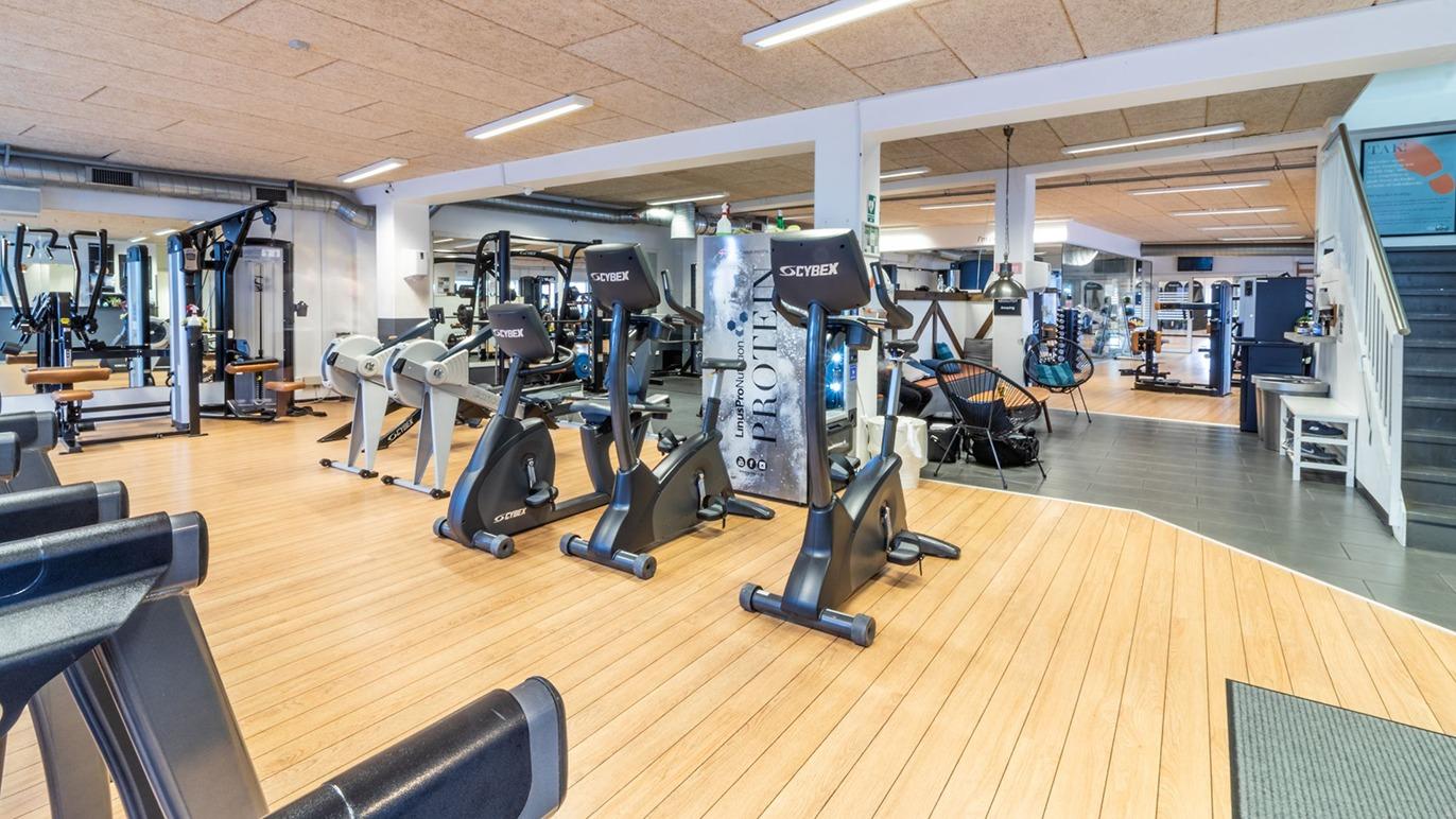 Et moderne fitnesscenter med træningsmaskiner og cardioudstyr på et lyst trægulv.