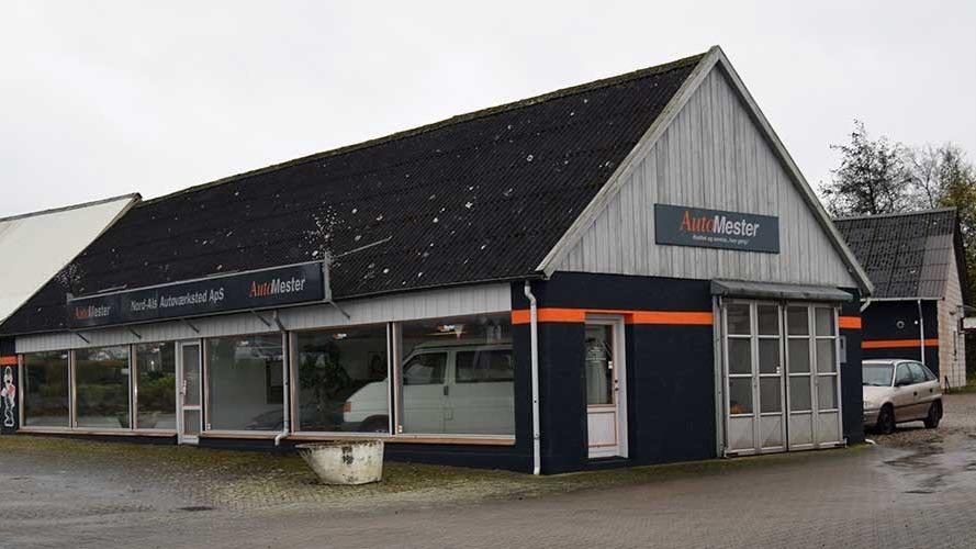 En bygning med grå træfacade og sorte detaljer, der huser en bilforhandler med store vinduer.