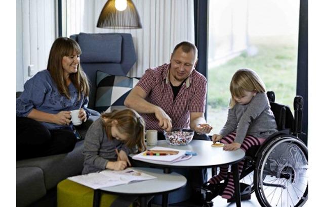 Familie sidder sammen i stuen, hvor børnene tegner, mens forældrene drikker kaffe og deler snacks.