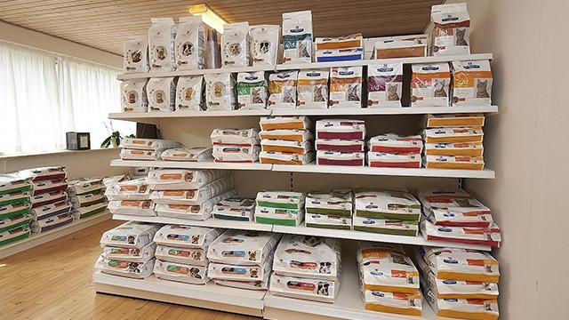 Hylder fyldt med farverige pakker af dyrefoder i en butik, der tilbyder forskellige typer foder til kæledyr.