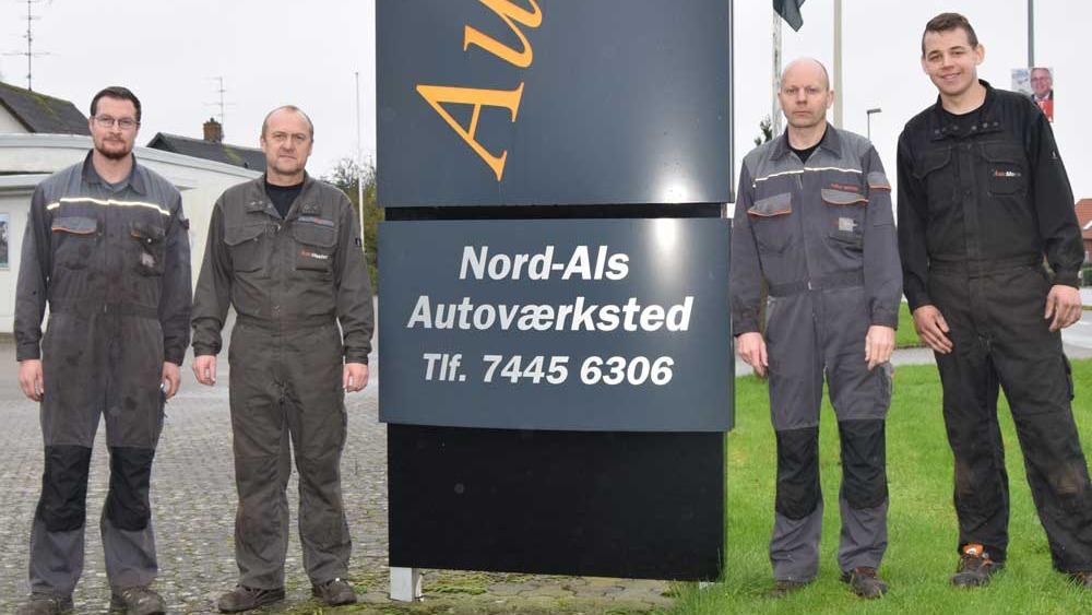 Fire mekanikere står foran skiltet til Nord-Als Autoværksted med kontaktinformation.