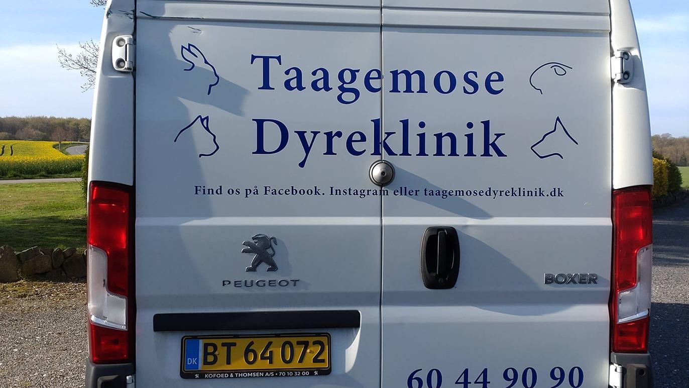 En hvid varevogn med teksten "Taagemose Dyreklinik" og kontaktinformation på bagsiden.