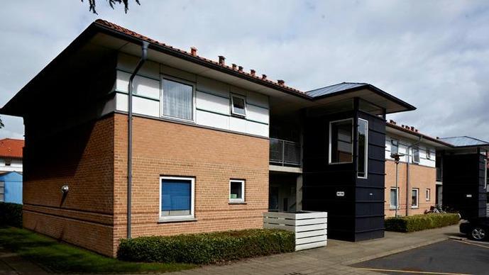 Moderne lejlighedskompleks med murstensfacade og sorte detaljer under en skyet himmel.