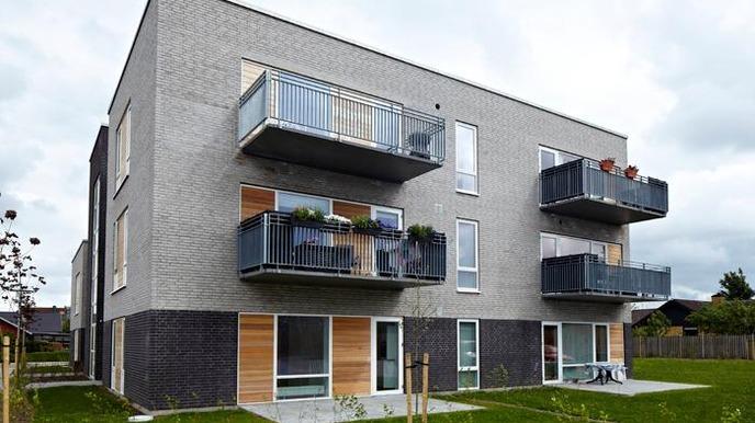 Moderne lejlighedsbygning med altaner og grønne områder omkring.