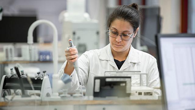En kvinde i laboratoriefrakke arbejder med en pipette i et moderne laboratorium.