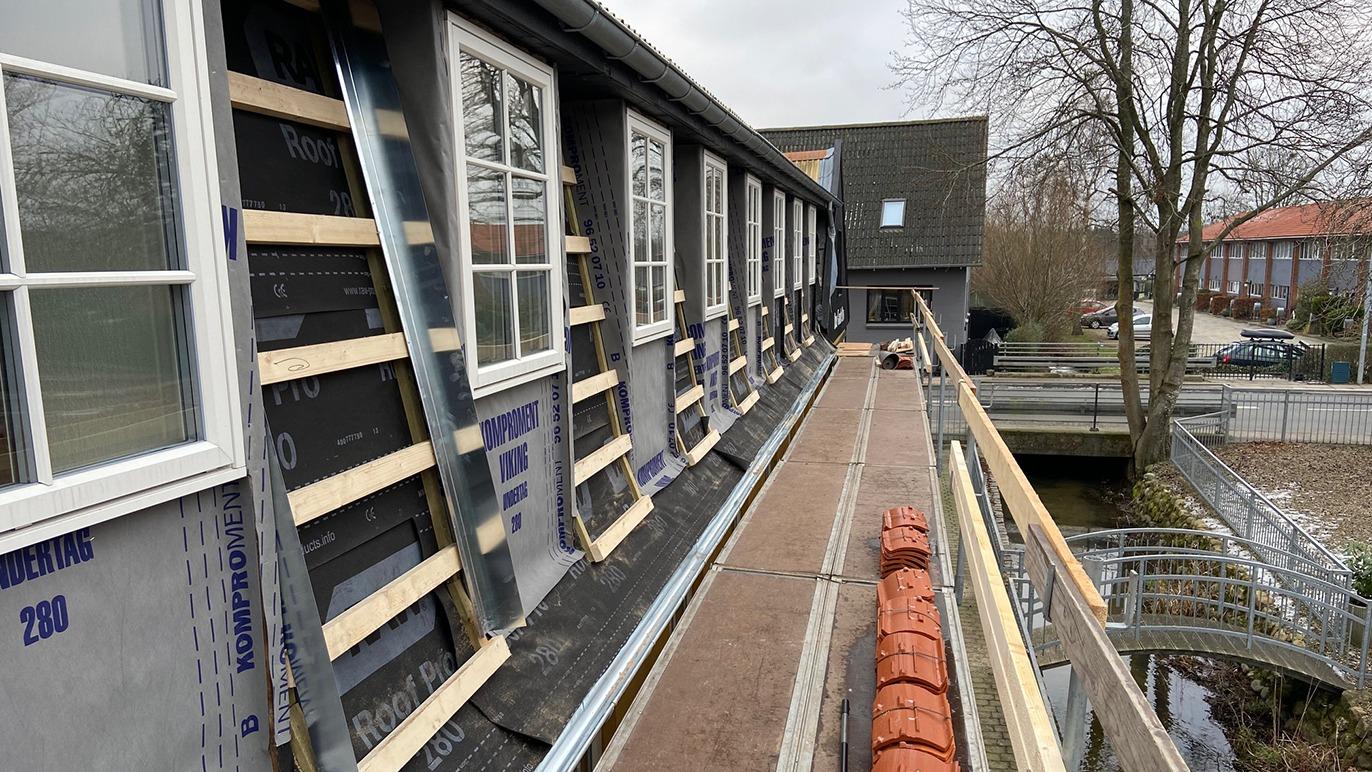 Billede af en bygning under renovering med vinduer, tag og stillads langs en gangbro.