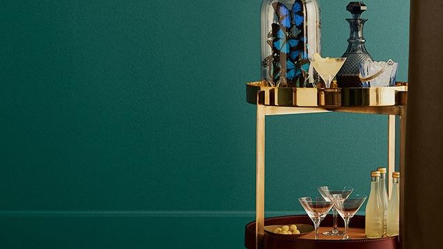 En elegant barvogn med glas, flasker og dekorationer på en grøn væg.