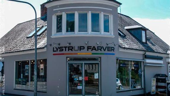 Facade af Lystrup Farver med store vinduer og farverig skiltning på bygningens front.