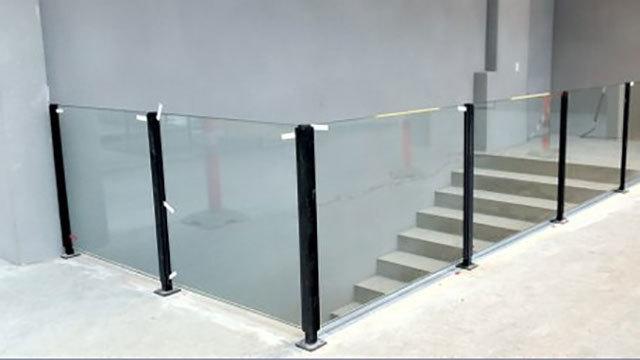 Glasgelænder ved trapper, der viser en moderne indretning med sorte metalstænger og en minimalistisk stil.