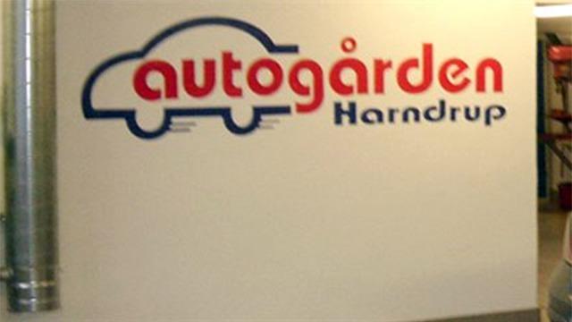 Vægskilt med teksten "autogården Harndrup" og en bilsilhuet i rød og blå farve.