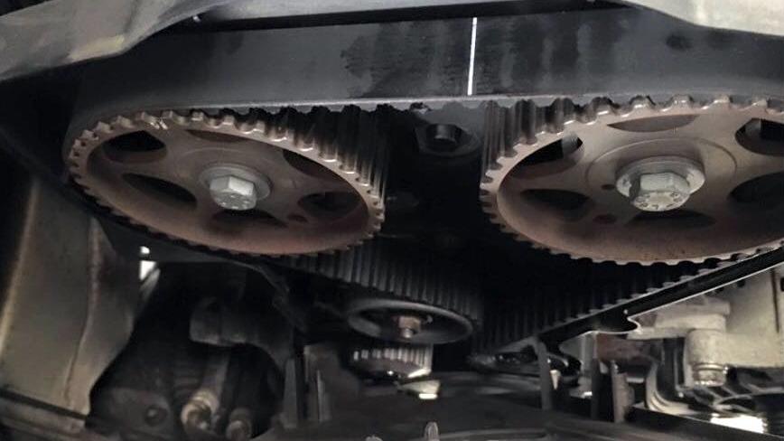 Tohjul og remskiver under en bilmotor, viser detaljer af tandremssystemet.