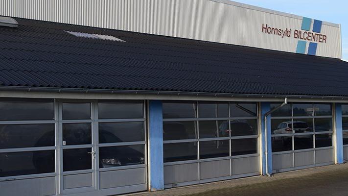Facade af en bygning med vinduer og et tag, der har et skilt med teksten "Hornslet Blæsercenter".