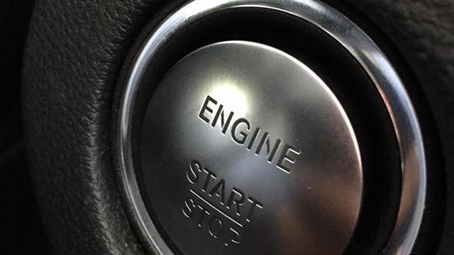 Nærbillede af en bils startknap med teksten "ENGINE START STOP" indgraveret.