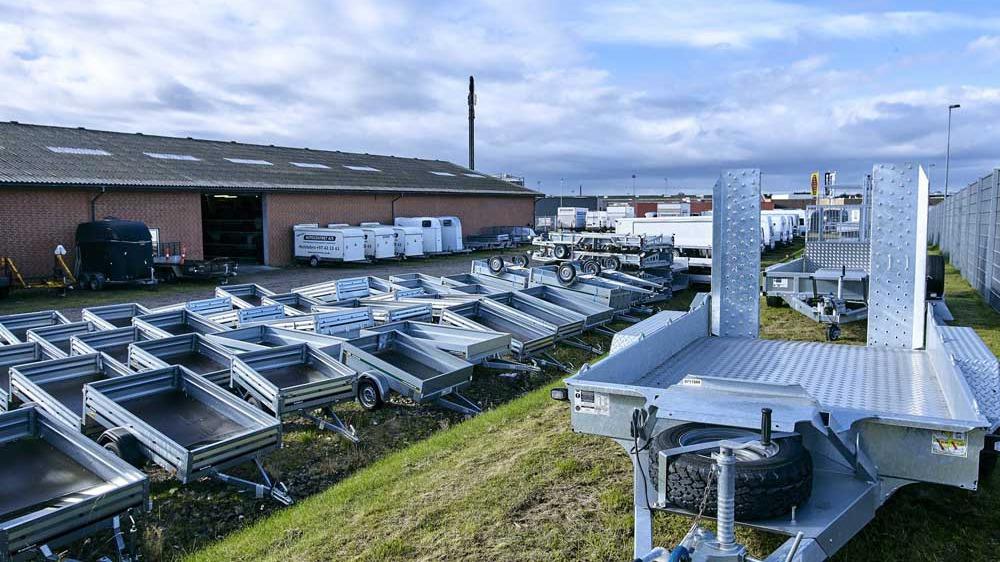 Lagerplads med flere trailere og en bygning i baggrunden under en skyet himmel.