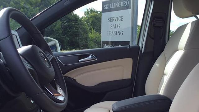 Interiør af en bil med beige sæder og rat, med en skiltebaggrund for bilservice og leasing.