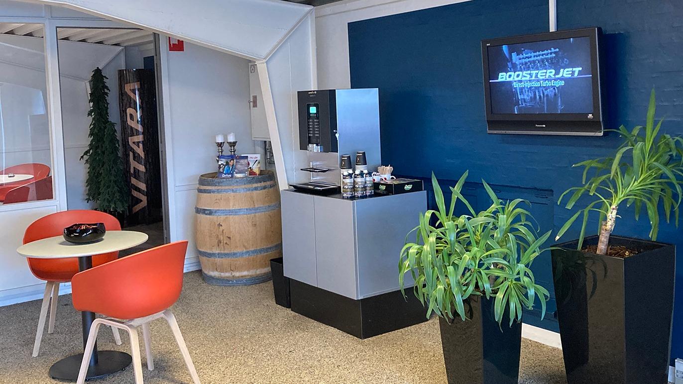 Moderne kontorindretning med kaffemaskine, planter og tv i et lyst rum med blå væg.