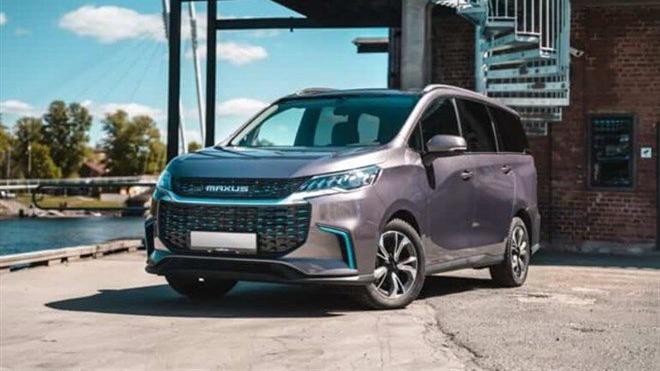 En moderne MPV parkeret ved en bygning nær vandet, med en stilfuld grå farve og sporty design.