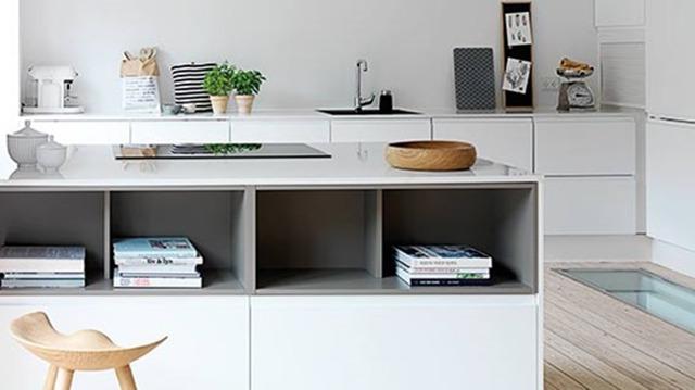 Moderne køkken med en ø, bøger, planter og minimalistisk indretning i lyse farver.