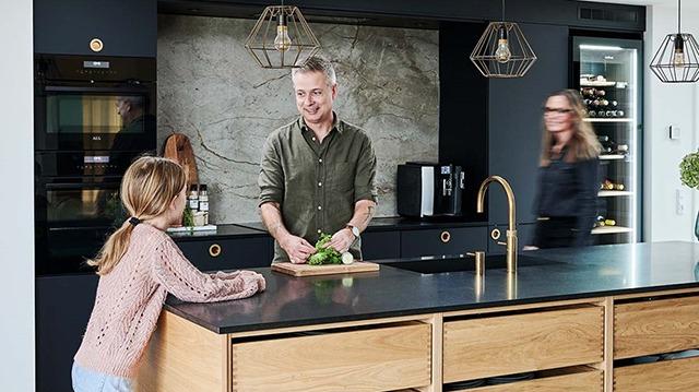 Far og datter laver mad sammen i et moderne køkken med en træø og stilfulde lamper.