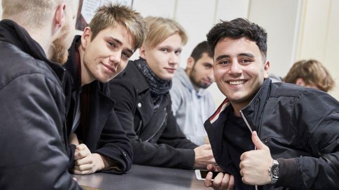 Gruppe af unge mænd, der smiler og sidder ved et bord i et uformelt miljø.