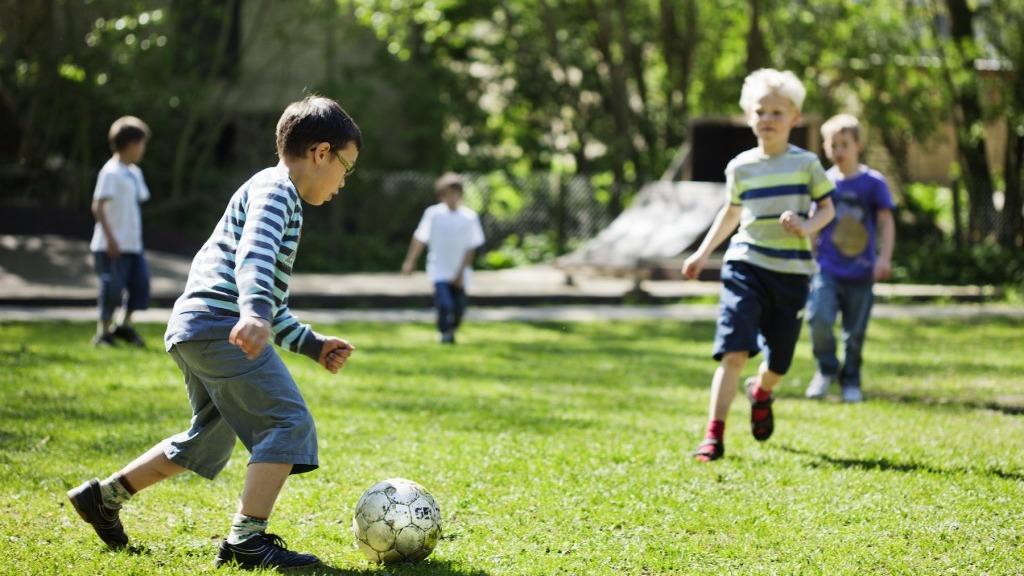 Børn spiller fodbold på en grøn græsplæne en solrig dag i parken.