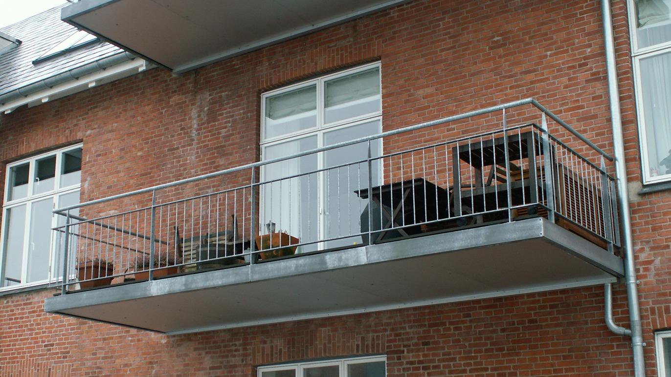 En balkon med planter og en hund, der står på gelænderet, ved en murstensbygning.