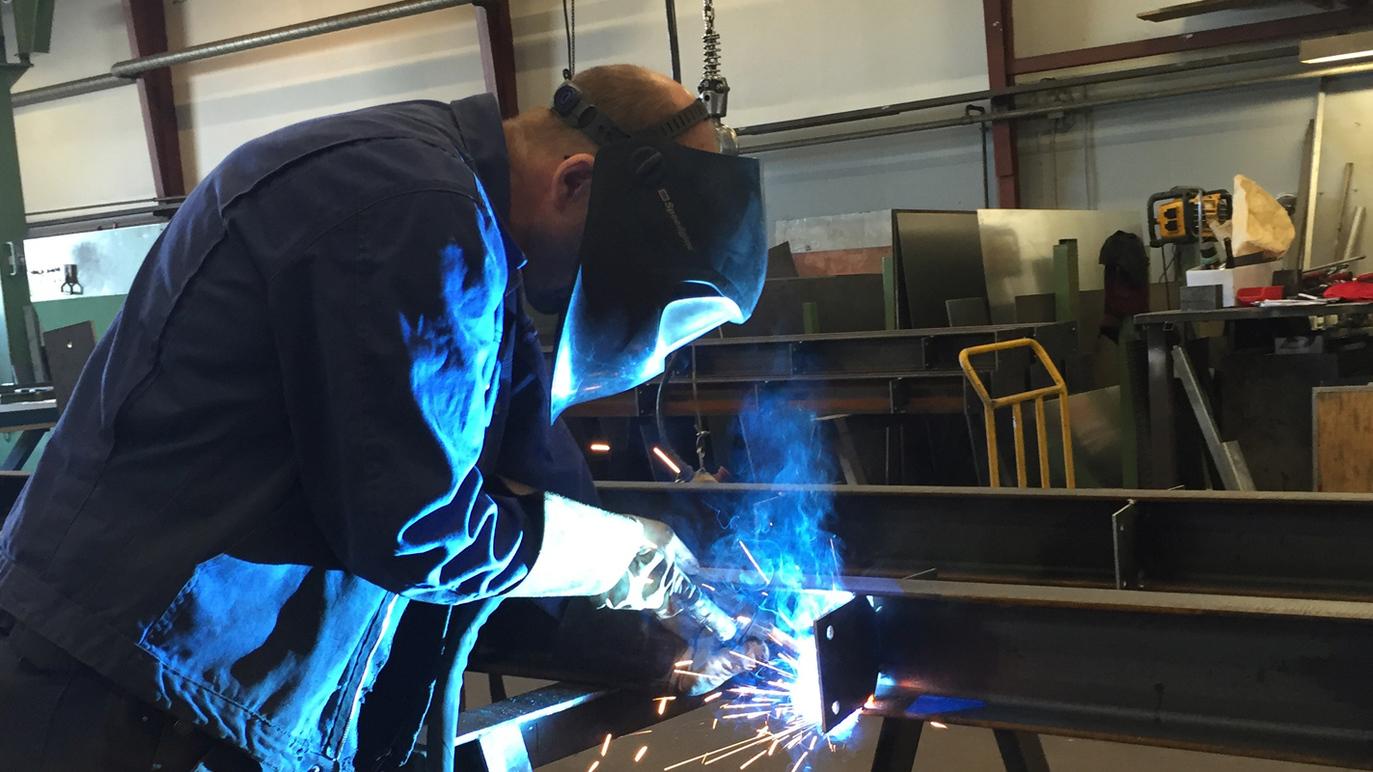 En svejser arbejder med en svejsemaskine, mens gnister og lys stråler fra svejseprocessen i en værksted.