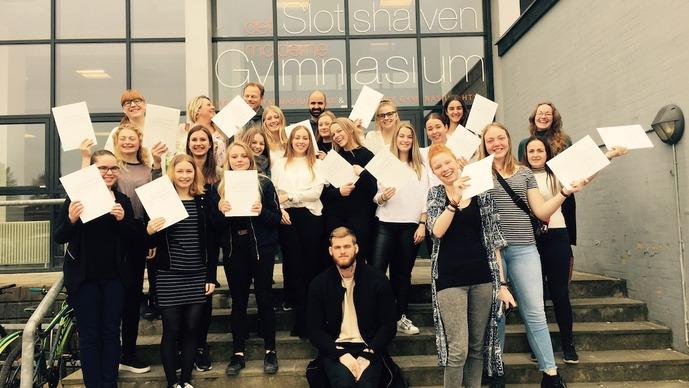 Gruppe af glade studerende, der holder deres eksamensbeviser foran gymnasiet.