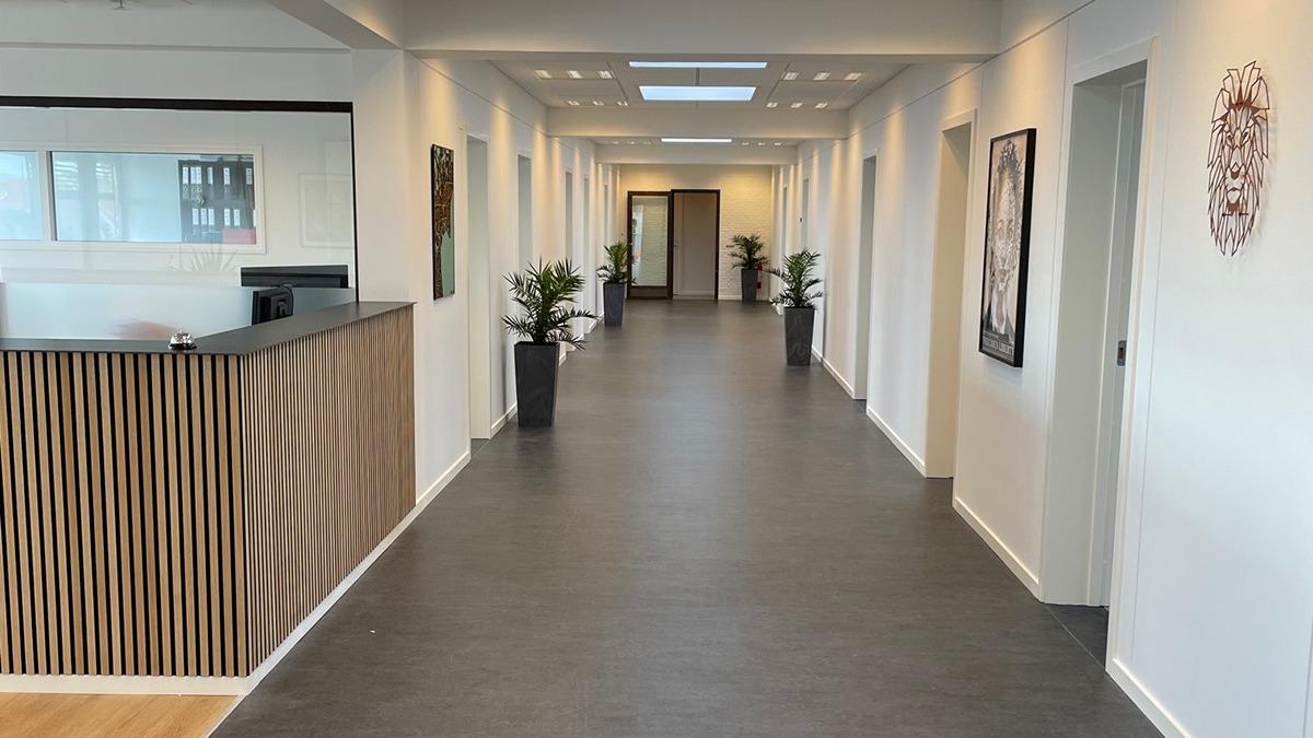 Moderne kontorindretning med en lang gang, reception og planter i potter langs væggene.
